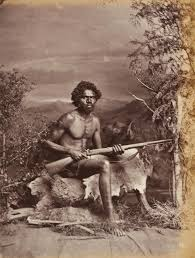 Old posed black and white photograph of Aboriginal may, seated, holding a rifle.
